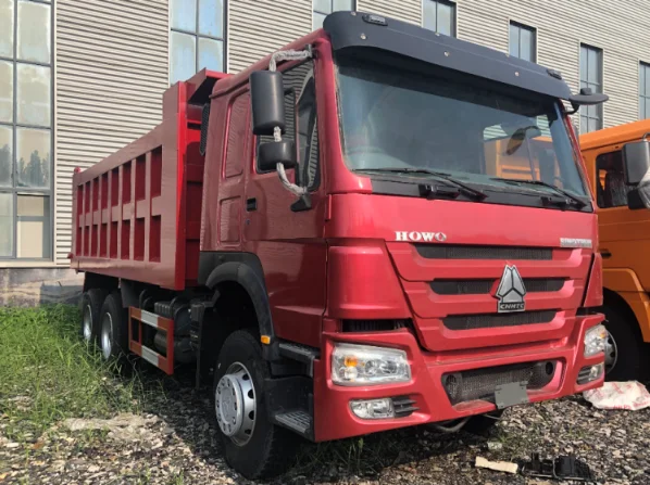 Red refurbished HOWO dump truck with a modern design, parked outside a warehouse, showcasing the front and side view.
