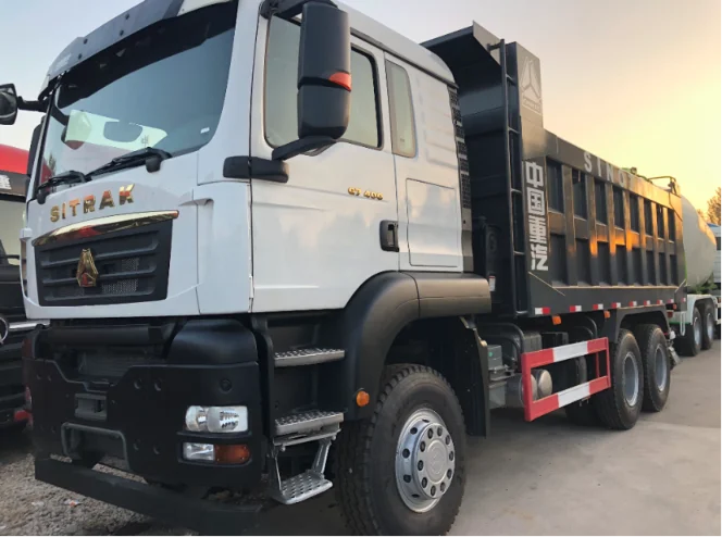 White SITRAK dump truck with a black cargo bed, showcasing the front and side view, parked in a lot with a sunset in the background.