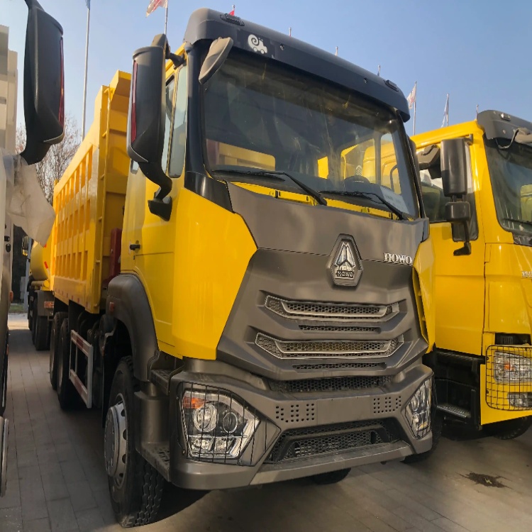 A yellow HOWO dump truck with a dark gray front grille parked at a truck dealership, surrounded by other